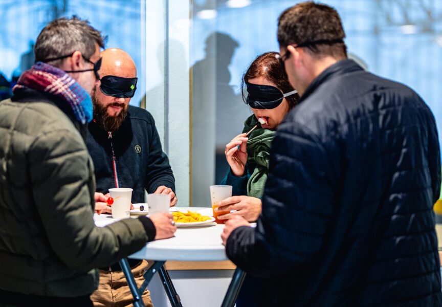 quatre personnes ont les yeux bandés et goûtent une brochette de jambon, mozzarella et tomates cerises à l'aveugle.