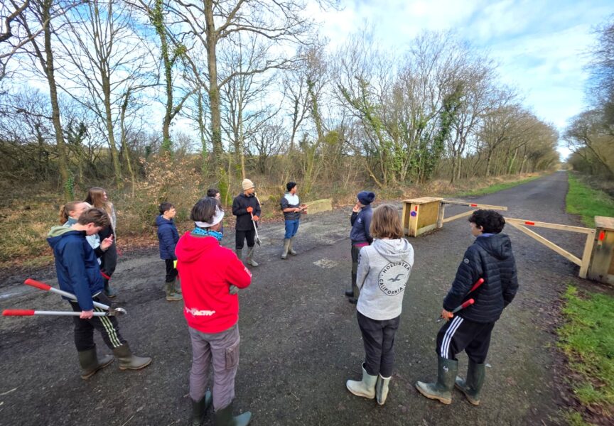 briefing du groupe de jeunes sur la route des Landes de la Poterie. 11 personnes sont sur la photo, en cercle à l'écoute des consignes. Ils ont des tenues adéquat au jardinage.